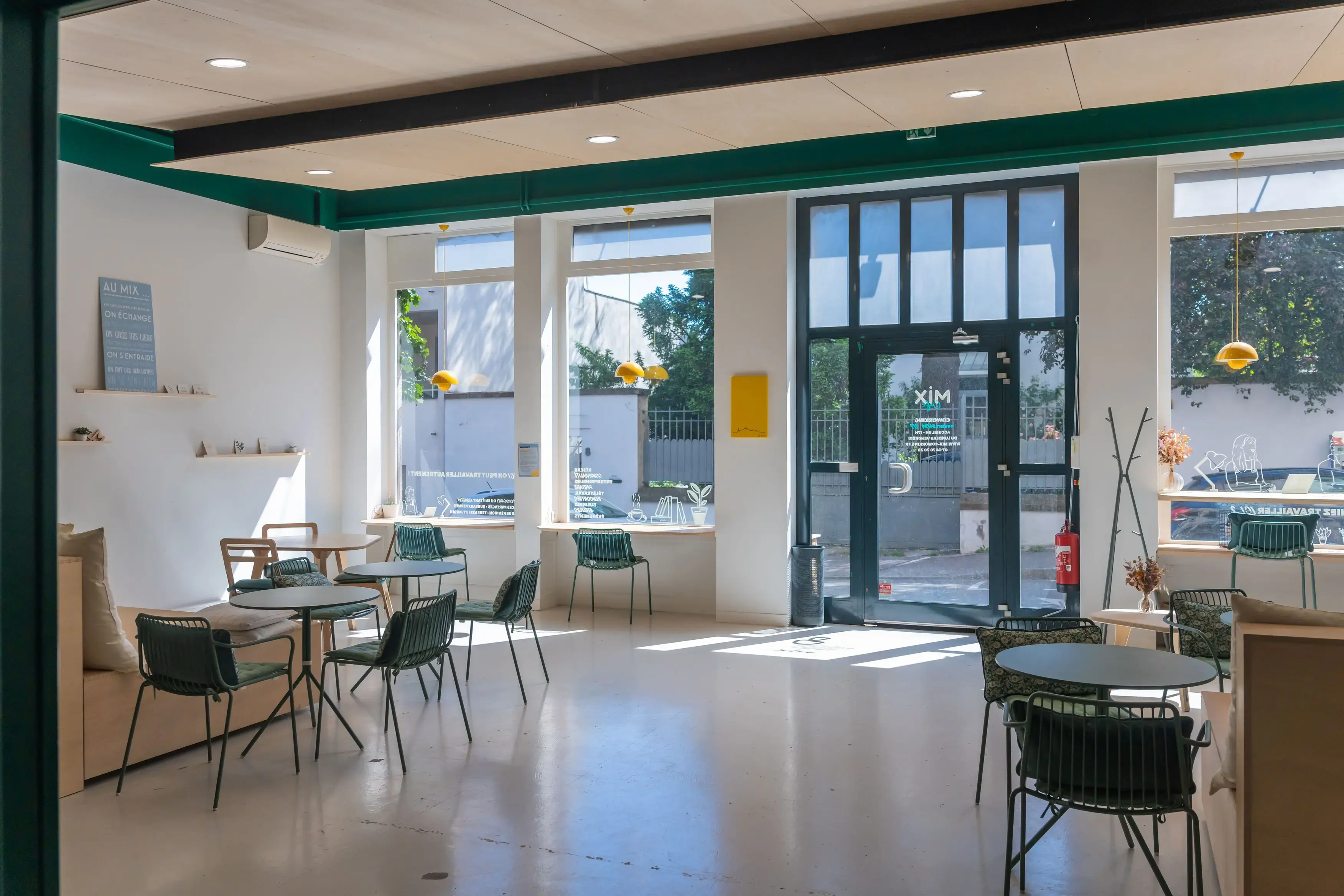 Espace de travail ouvert du MIX Café, large espace avec grande fenêtre, tables rondes et chaises de café vertes, grande hauteur sous plafond
