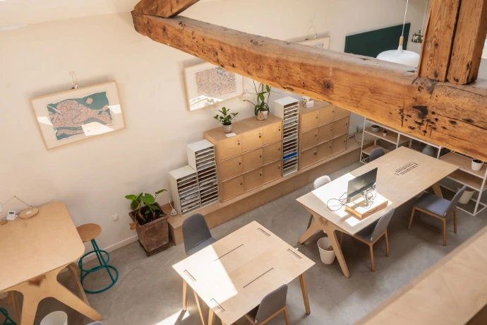 Open space du MIX Coworking vu d'en haut, poutres et larges tables en bois vus d'un haut avec casier longeant le mur et tableaux aux murs.