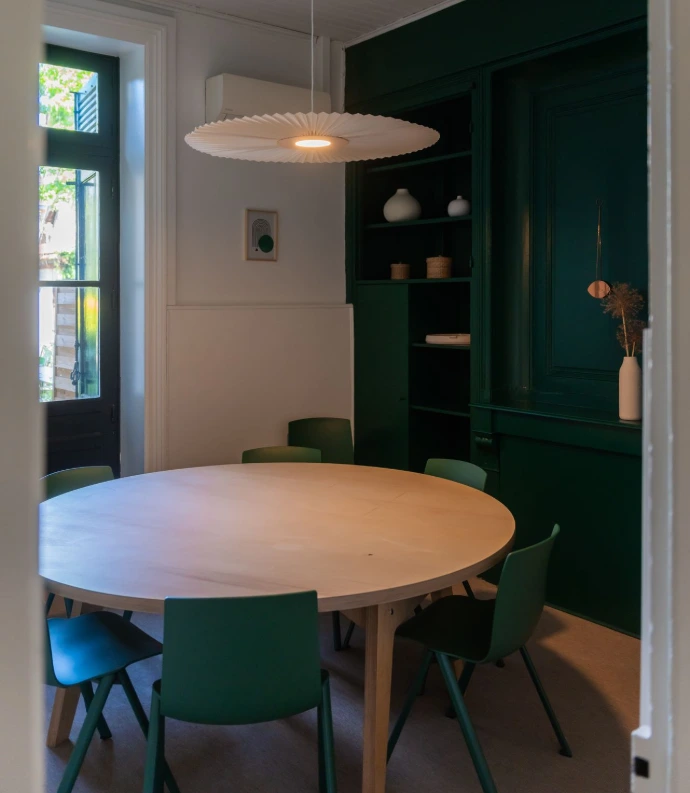 Salle de réunion Le Jardin Vert vu de la porte d'entrée, table ronde en bois massif avec chaises vertes autour, avec grande fenêtre donnant sur le jardin.