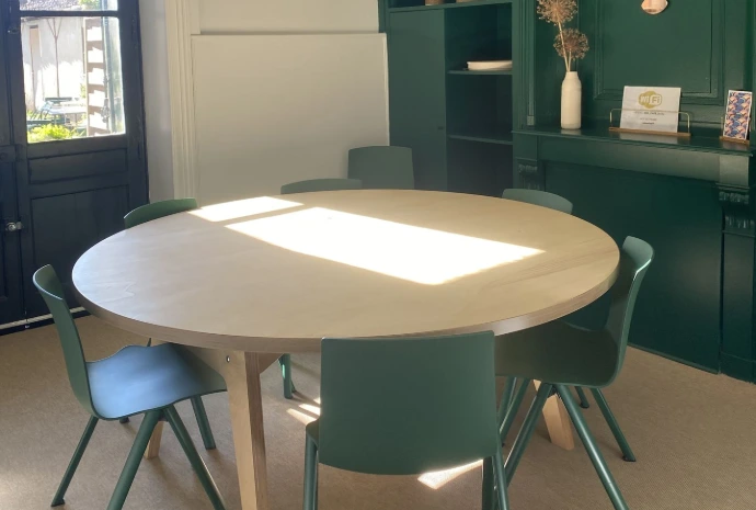 Salle "Le Jardin", photo de la table ronde au milieu avec 6 chaises autour, grande fenêtre à gauche et mur signature vert foncé avec vidéoprojecteur