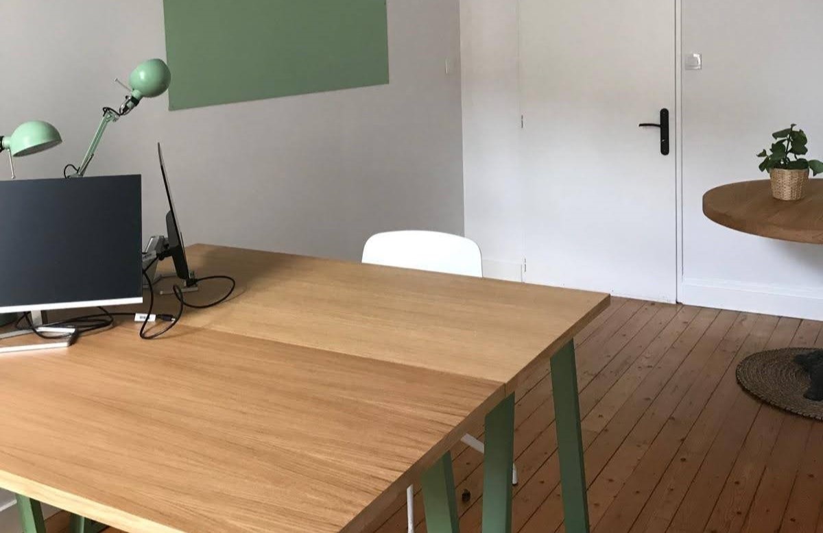 Bureau spacieux avec deux grandes tables collées, un meuble de rangement et une table ronde